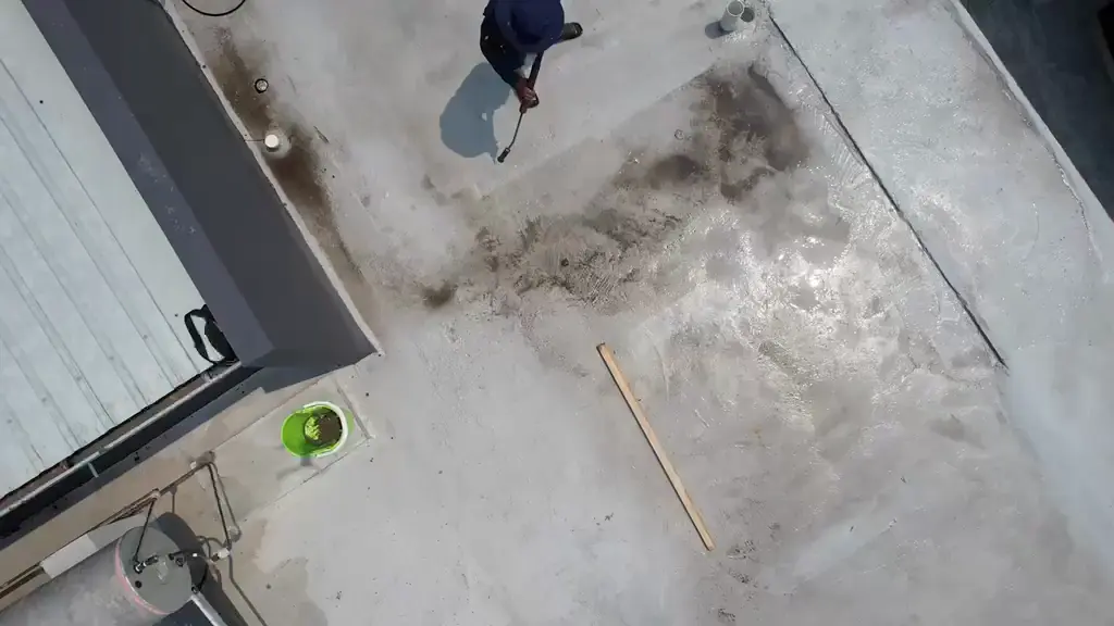 Overhead view of a worker washing a grey flat roof with a hose