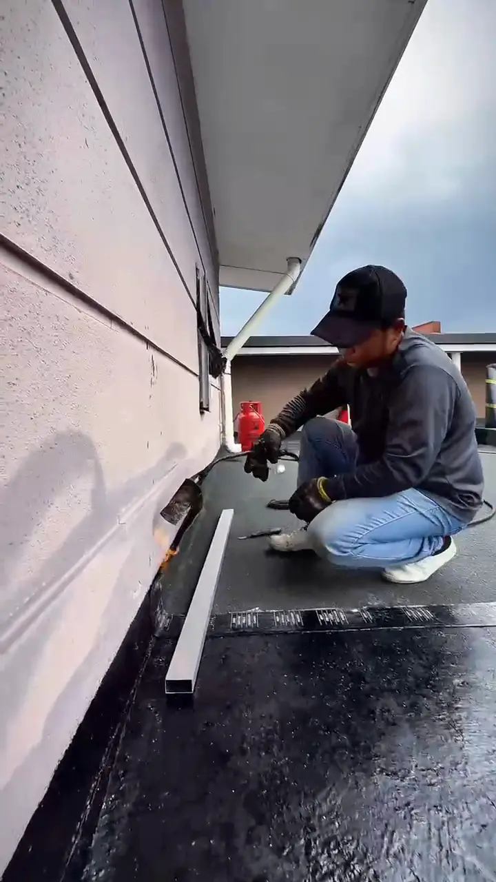 Worker crouching at the base of a wall on a flat roof, working on the membrane edge