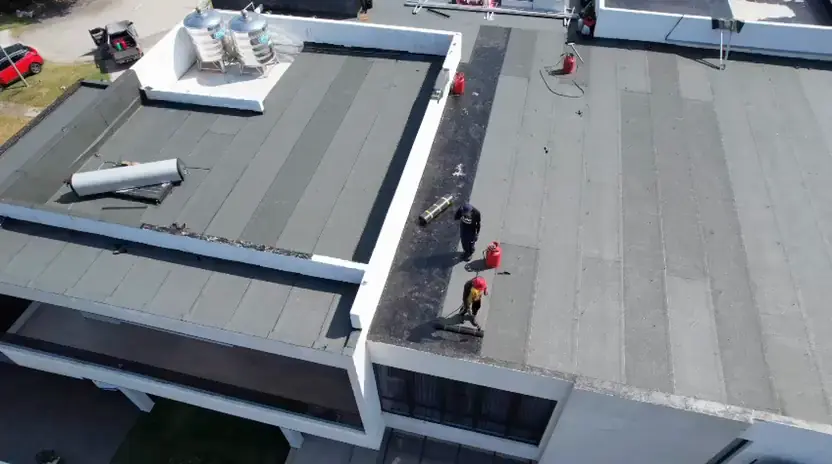 Aerial view of a wide flat roof with membrane strips and workers