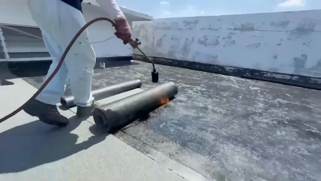 Worker's legs and a torch heating a black membrane roll on a flat roof